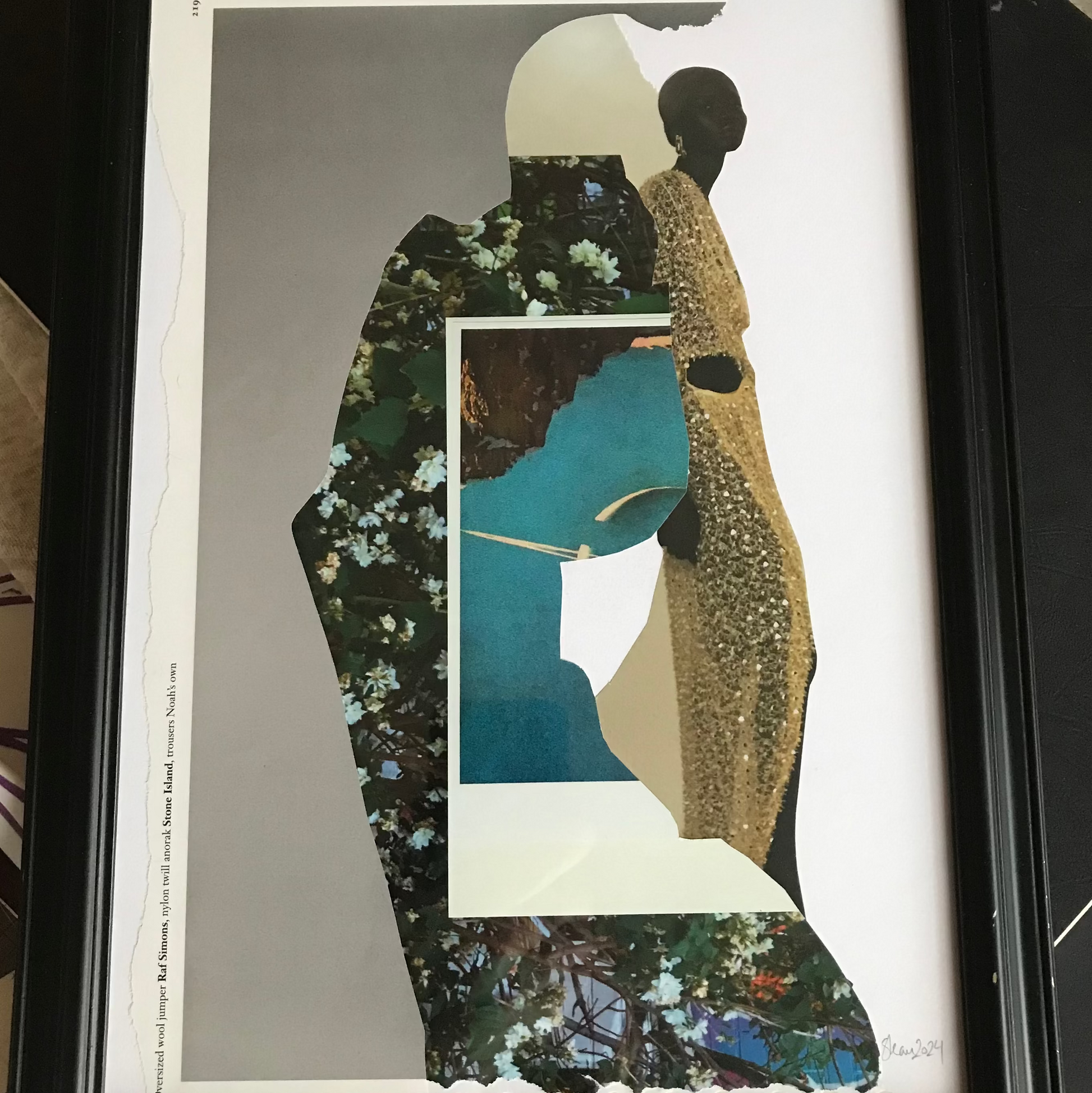 A framed art print featuring a stylized collage of two human silhouettes in floral and leopard-print patterns, with a central teal and cream geometric shape, displayed in a black frame on a desk.